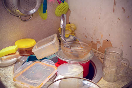 Dirty dishes dumped in a sink in a poor, worn kitchenの写真素材
