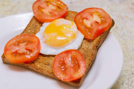 Toast bread with fried egg and chopped tomatoes on a white plate.の写真素材