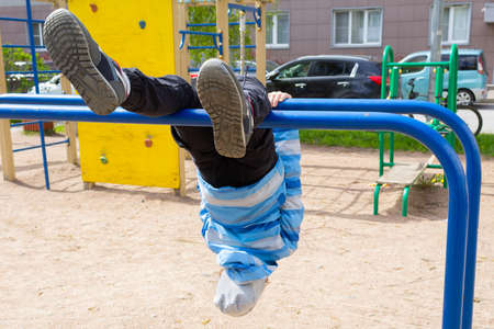 A child in the playground hanging on the bars upside down. Soles of sneakers in the foreground.の写真素材