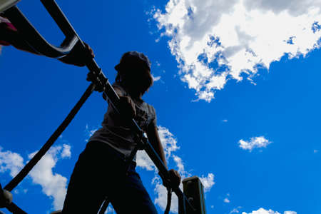 Dark silhouette of child against blue sky and white clouds. Entertainment at the playground. Soft focusの写真素材