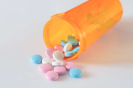 Orange prescription bottle with scattered out colored pills on a white background. Soft light.の写真素材