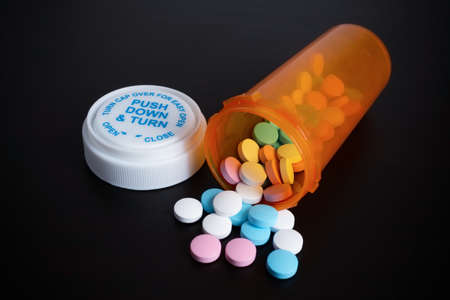 Orange prescription bottle with safety cap and scattered out colored pills on dark background.の写真素材