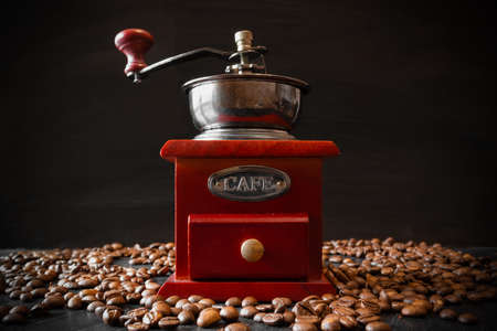 Retro wooden coffee grinder and coffee beans on dark background.