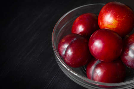 Red plums in transparent bowl on dark background. Close-up.の写真素材
