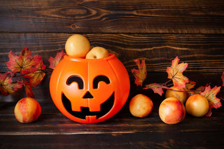 Halloween pumpkin basket with nectarines inside and around, autumn leaves on wooden plank surface.の写真素材