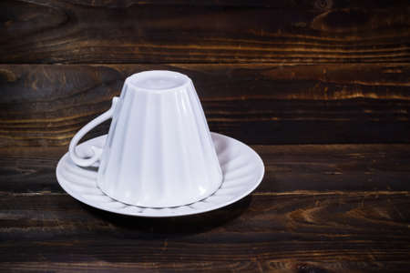 White porcelain cup turned upside down on saucer, on dark brown wooden surface.の写真素材