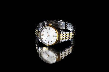 Shiny metal wrist watch on mirror surface on black background. Close-up.の写真素材