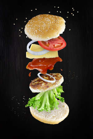Levitating cheeseburger ingredients on dark background. Burger components floating in the air: cheese, ketchup, onion, cutlet, tomato, lettuce, ketchup.の写真素材