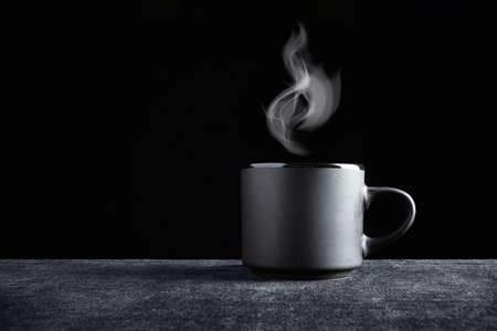 Black cup with steam over it on dark surface and black background.の写真素材