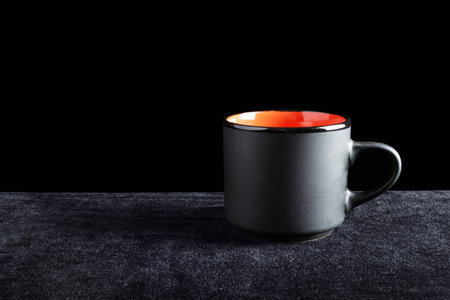 Black cup colored orange inside on dark surface and black backgroundの写真素材