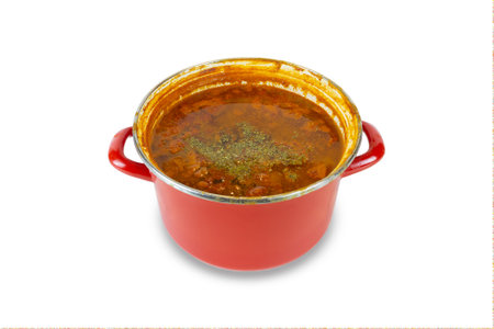 Orange soup with seasoning in red saucepan, isolated on white background.の写真素材
