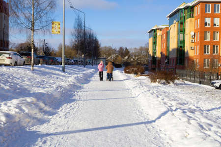 Snowy street with houses, trees and cars. Two women walking in the distance. - Russia, St. Petersburg, February 2021.のeditorial素材