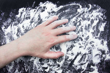 Hand on white flour scattered on black surface.