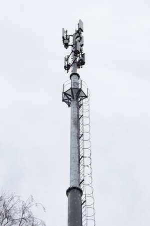 Cell tower on background of gray sky and tree branches.の写真素材