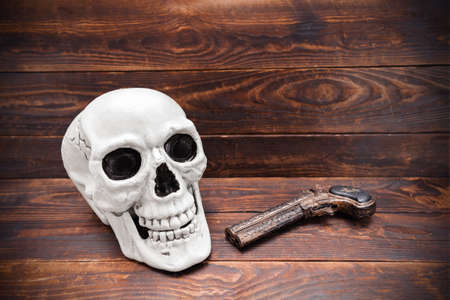 Human skull and vintage carved pistol on wooden plank surface.の写真素材