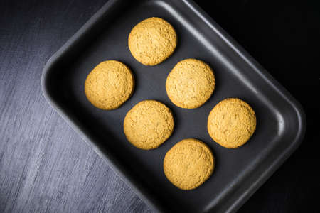 Six round baked biscuits on black oven-tray, view from aboveの写真素材