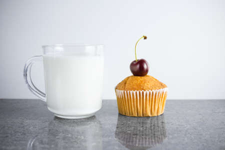 Cupcake with cherry on top and transparent cup of milk on gray granite tableの写真素材