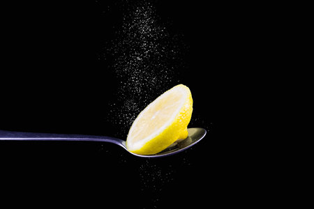 Lemon slice on metal spoon with dripping white powder from above on black backgroundの写真素材