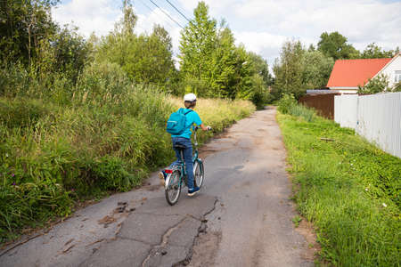 Boy on bike on village road with green trees from the backの写真素材