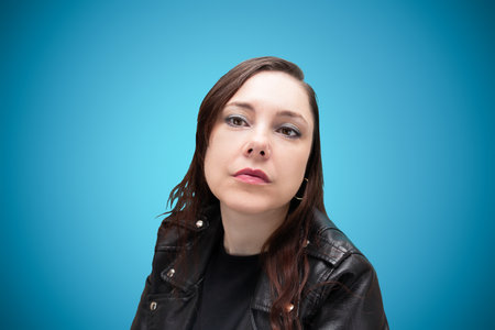 Serious woman in black biker jacket with loose hair, heavy metal style, on blue backgroundの写真素材