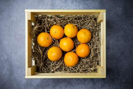 Wooden box with fresh tangerines in paper shavings on gray surface, view from above, flat layの写真素材