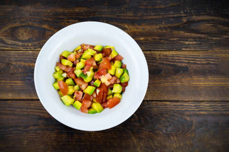 White plate with avocado and tomato salad on brown wooden surface, top view, flatlayの写真素材