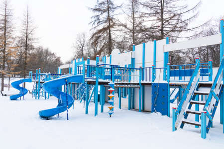 Blue snow covered large empty playground with stairs and slides among coniferous treesの写真素材