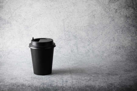 Black paper disposable cup with plastic lid on gray surfaceの写真素材