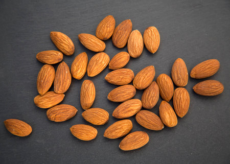 Raw Natural Organic Almonds Nuts Scattered Isolated on Black Shale Background Top View Healthy Food for Life Natural Light Selective Focusの写真素材