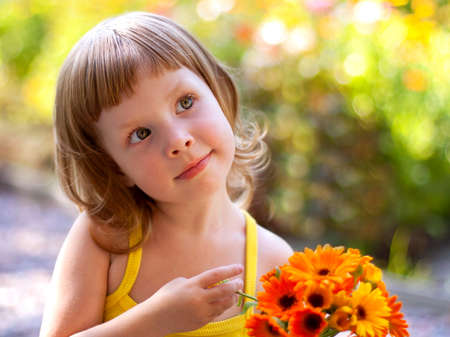 Cute little girl with a bouquet of flowers in the summer on the street carefully looks at someoneの写真素材