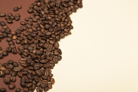 Scattered roasted coffee beans on beige and brown backgroundの写真素材
