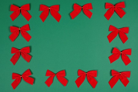 Twelve cute red bows with golden elements on green background laid as a frame for text. Christmas and New Year background.の写真素材