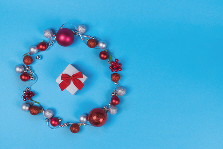 Christmas wreath made of silver ribbon, vibrant red and silver baubles on blue pastel background and little gift box with cute bow. Copy space.の写真素材