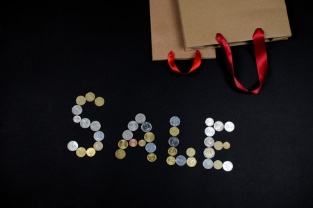 The word Sale written with coins and two paper bags with red silky handles on black background. Black Friday concept.の写真素材