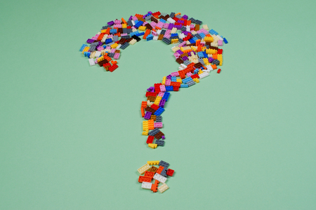 Question mark of scattered colorful plastic construction toys on light green background.