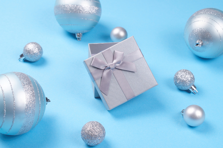 Composition of beautiful open silver gift box with cute silky bow and shiny Christmas baubles blue pastel background. New Year and Christmas celebration concept.の写真素材