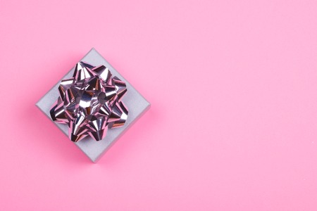 Top view of a beautiful little gift in a light blue box with shiny silver bow on trendy pink pastel background. Festive and celebration concept.の写真素材