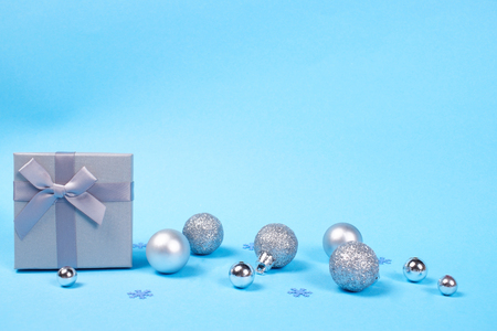 Composition of beautiful gift box with cute silky bow and shiny Christmas baubles on blue pastel background decorated with snowflake confetti with copy space.の写真素材