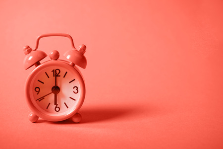 Analogue alarm clock showing six in the morning on background of Living Coral color of the year 2019. Copy space.の写真素材