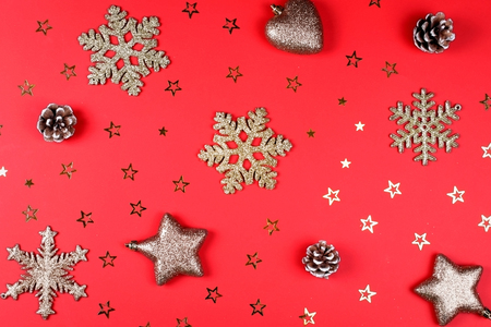 Christmas background of golden star confetti, glitter snowflakes, natural cones and decorative stars and heart on vibrant red backdrop.の写真素材