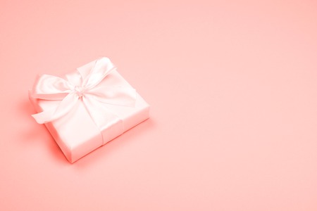 Beautiful little gift box with silky bow on trendy pastel coral background. Main trend of the year 2019. Festive and celebration concept.の写真素材