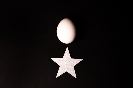 White egg and glitter star on black background.の写真素材
