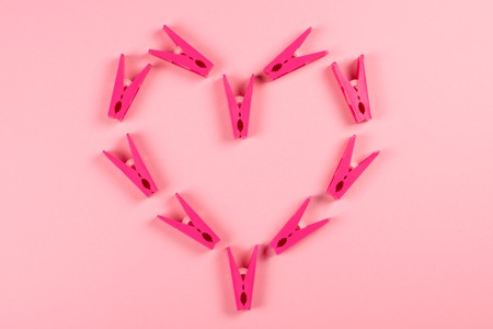 Magenta plastic clothespins arranged forming a heart on pink of background. Love and Valentine's Day concept.の写真素材