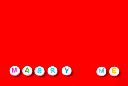 Lettering Marry Me made of white beads on vibrant red background with copy space. Couple, engagement...