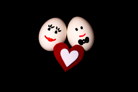 Couple of loving smiling mister and missis eggs and a felt fiber heart on dark black background. Love and Valentine's day concept. Easter and Holiday concept.の写真素材