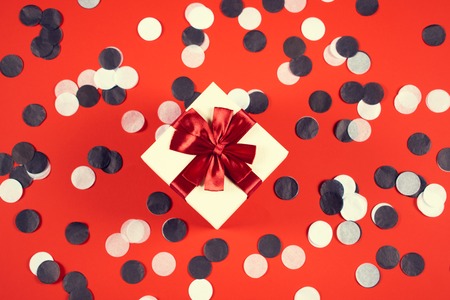 Beautiful present box on red background with confetti.