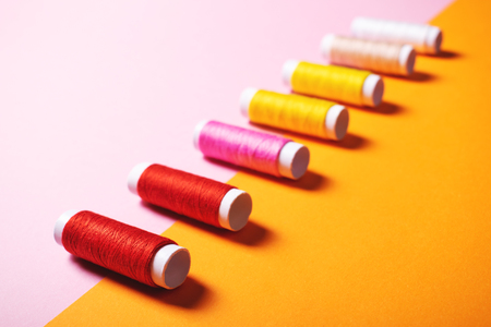 Close-up of set of colorful threads for sewing on bright double colored pink and orange background. Selective focus. Creativity and fashion concept.の写真素材