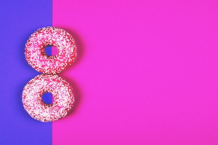 Two tasty fresh pink donuts on double colored pink and purple table forming number 8 with copy space for text or greeting.の写真素材