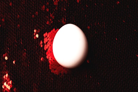 One white egg on background of vibrant red sequin. Disco fabrics. Selective focus. Easter and holiday concept.の写真素材