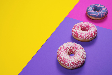 Three sweet colorful frosted donuts on bright multi colored background with copy space for text. Sweet and fast food concept.の写真素材